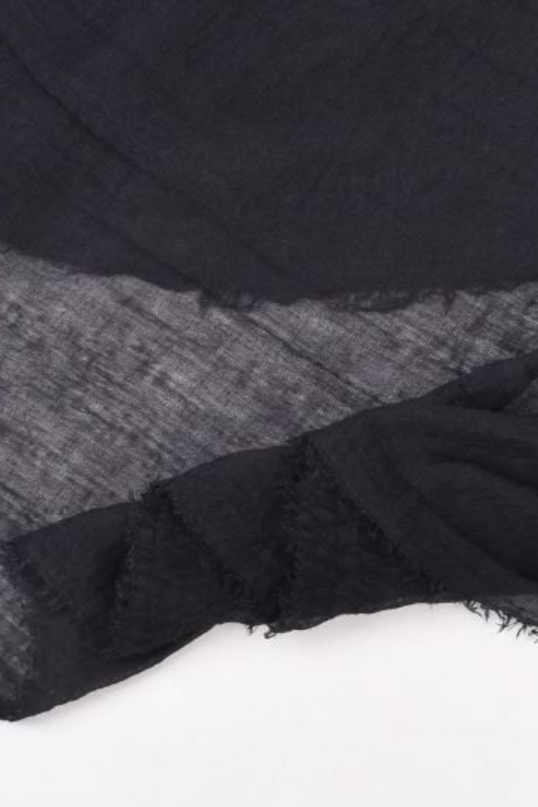 A close-up image of a piece of black, semi-transparent fabric with a frayed edge, resembling the delicate weave of a looselyboho Color-POP Scarf. The fabric appears to be layered, creating a textured appearance against a light background.
