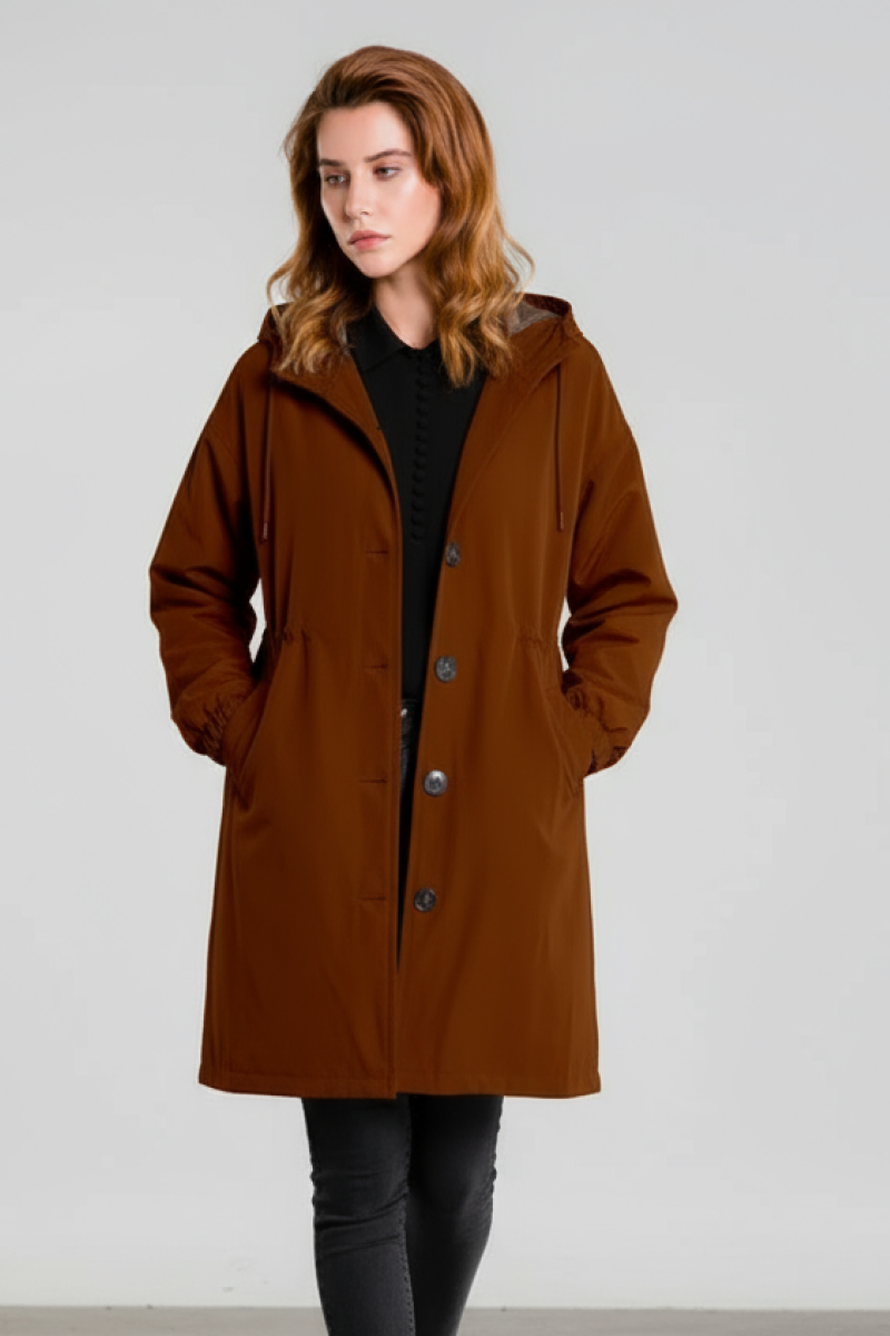 A woman stands against a plain background wearing the looselyboho BURNT BROWN WINDBREAKER with an adjustable hood and pockets, paired with black pants.