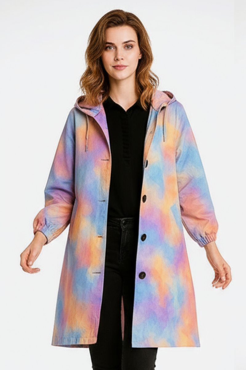A person wears the looselyboho CANVAS SKY WINDBREAKER, a knee-length, hooded jacket in pastel pink, blue, yellow, and orange tie-dye with black buttons. The water-resistant piece is styled with a black top and pants.