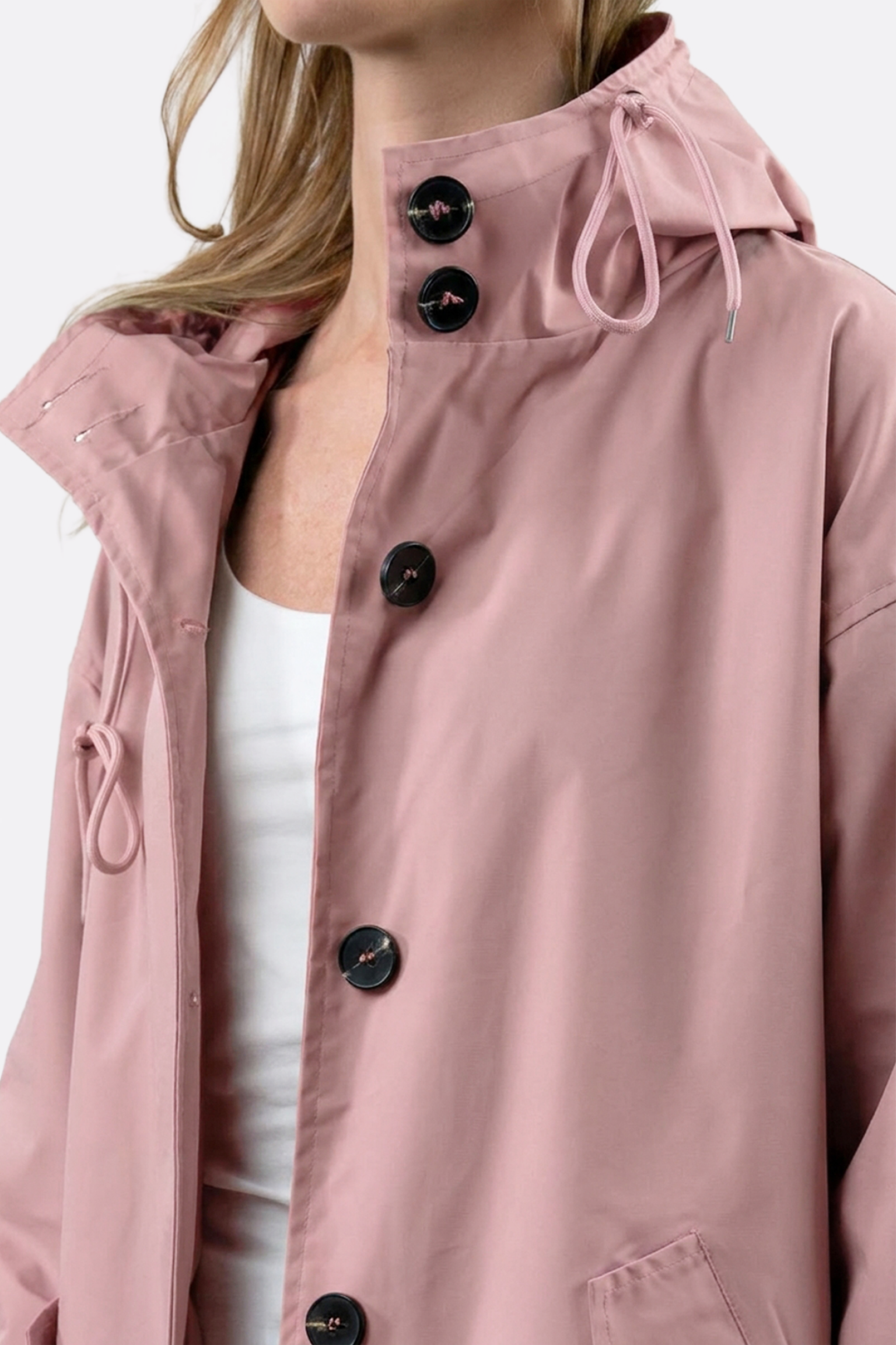 A person wears the Icon Windbreaker Rain Jacket in light pink with a hood and black buttons over a white top, shown from shoulders to waist against a plain background.