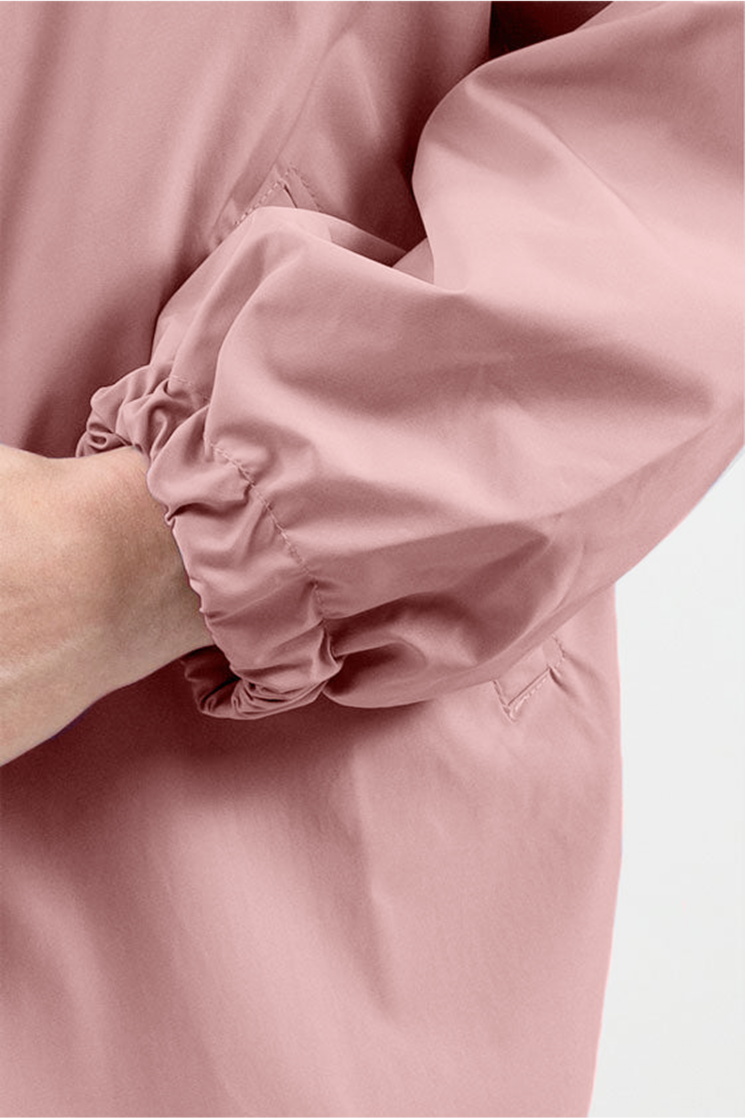 A close-up of a person’s arm wearing the Icon Windbreaker Rain Jacket in light pink with an elasticated cuff. The hand is partially visible against a plain, light background.