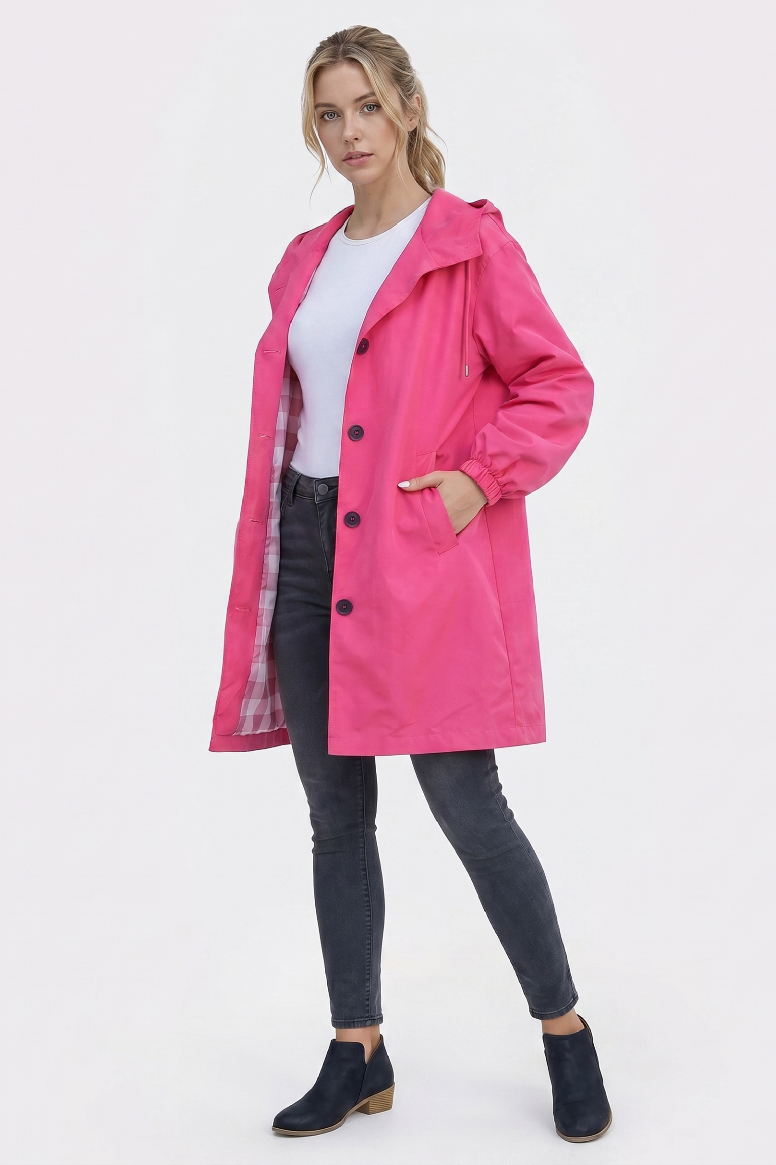 A person wears the Icon Windbreaker Rain Jacket in bright pink over a white shirt, paired with dark gray jeans and black ankle boots, standing with one hand in the jacket pocket against a plain light background.