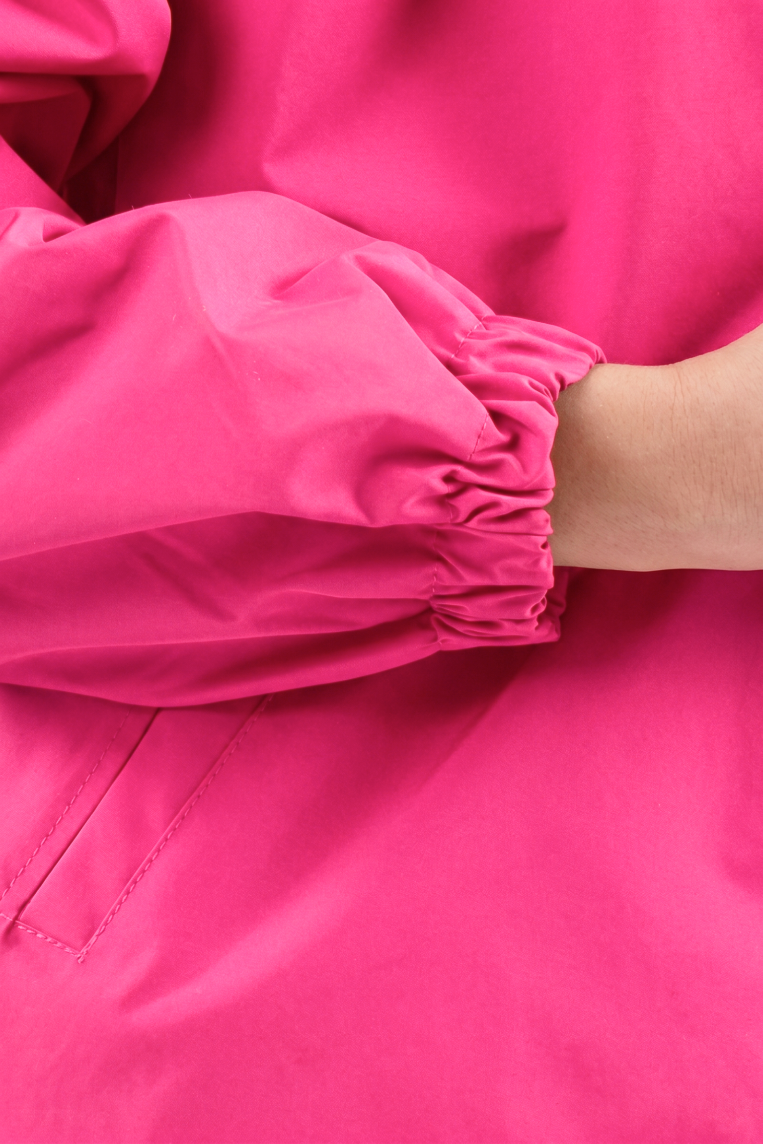 A close-up of a person’s arm wearing the Icon Windbreaker Rain Jacket in bright pink, featuring elastic at the wrist. The person's hand is partially visible, and the jacket’s fabric looks smooth and slightly shiny.