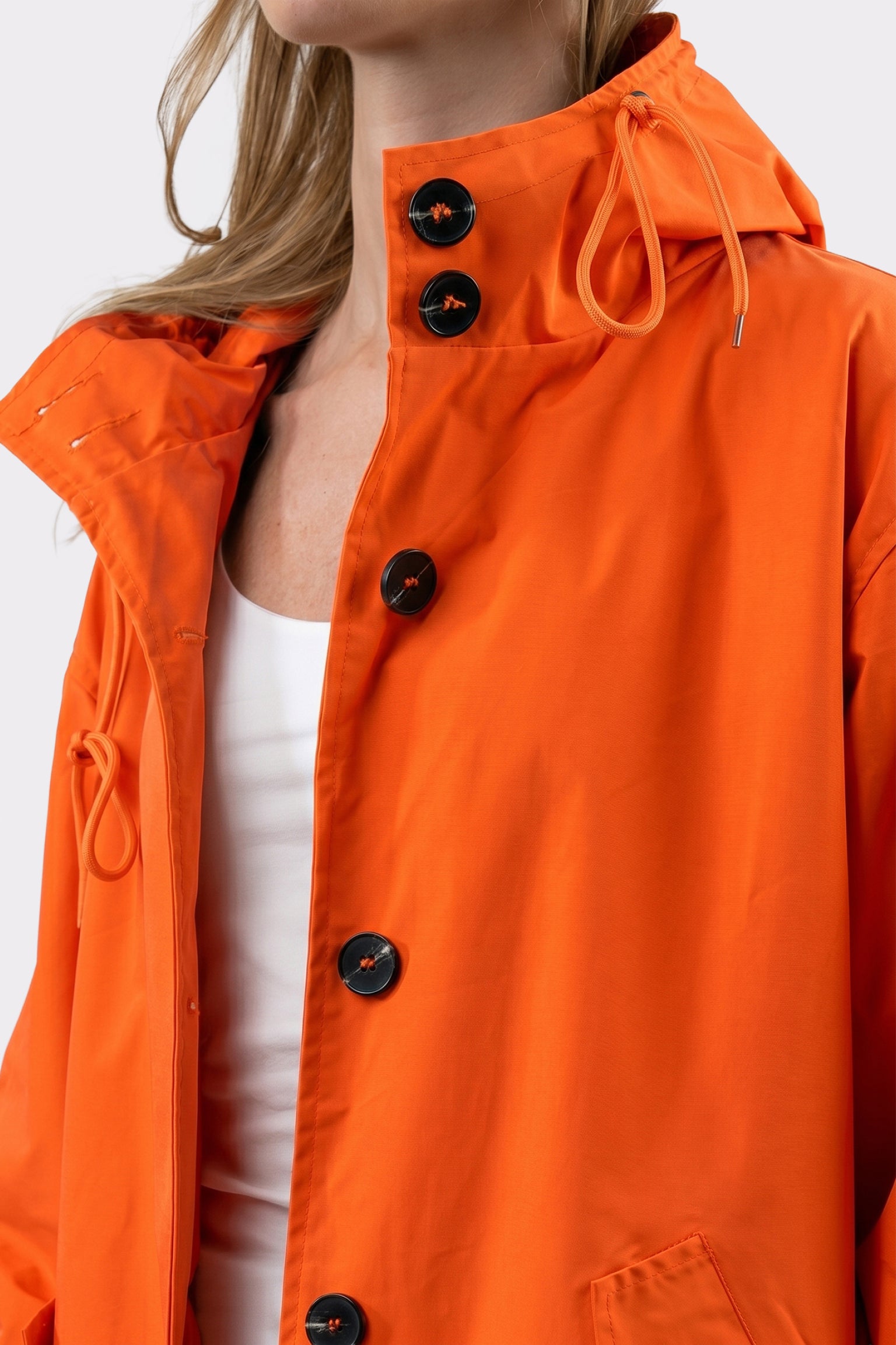 A person in a bright orange Icon Windbreaker Rain Jacket with large black buttons over a white top. The image is a close-up of the upper body.