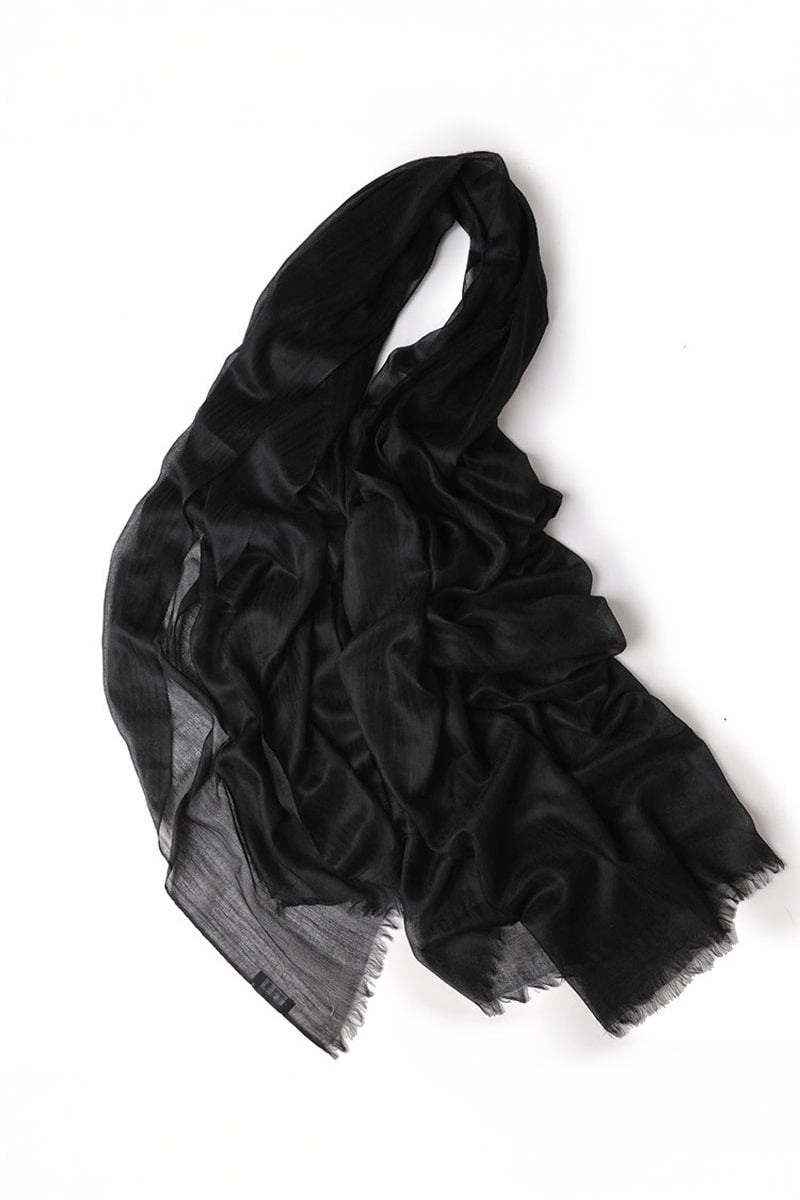 The looselyboho Noir Eclipse 100% Cashmere Scarf is a lightweight, semi-sheer black accessory with a subtle texture and gently frayed edges, adding effortless elegance to any outfit. Shown loosely arranged on a white background.