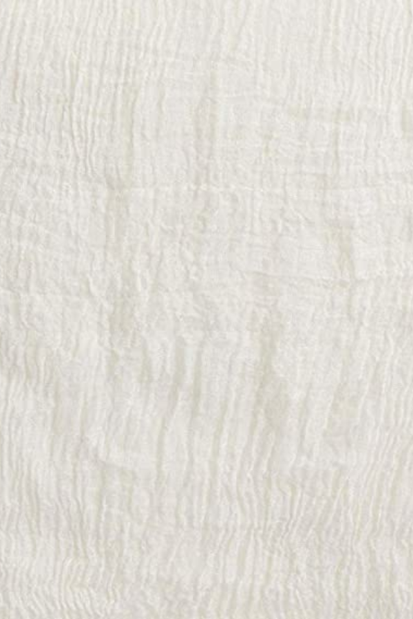 A close-up view of a white textile with a textured, wrinkled pattern. The fabric appears soft and slightly crinkled, much like a Color-POP Scarf from looselyboho, showcasing subtle vertical lines and folds throughout its surface.