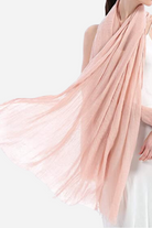 A person wearing a white sleeveless top is draped in an all-weather, light pink sheer looselyboho Color-POP Scarf that is blowing gently. The delicate fabric of the scarf appears soft and airy, creating a flowing, elegant look perfect for any season.