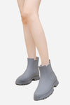 Close-up of a person's legs, wearing gray ankle-high Non-Slip Rain Boots with chunky SuperGrip soles by looselyboho. The background is plain white.