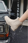 A person's leg in a pair of Non-Slip Rain Boots from looselyboho is being splashed with water, positioned near the front of a black vintage car. The water streams down the side of the waterproof Non-Slip Rain Boots, highlighting their water-resistant quality. The background shows a blurred sign with the word "VINTAGE.