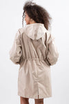 A person with curly hair is shown from the back wearing The WJacket's Water Resistant Oversized Hooded Windbreaker Rain Jacket in light beige. The jacket features a cinched waist and long sleeves. This timeless style stands out against a plain white background, showcasing its versatility for any wardrobe.