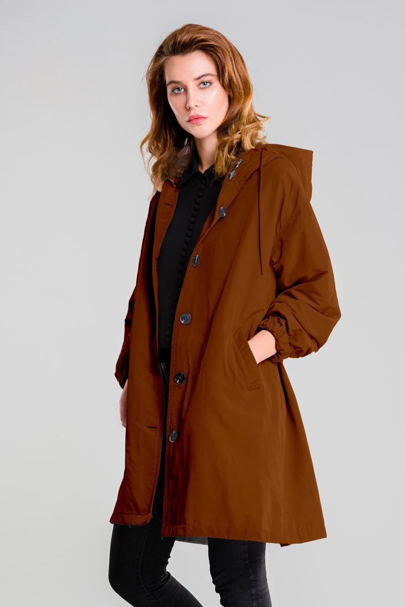 A person with shoulder-length hair wears the looselyboho BURNT BROWN WINDBREAKER with an adjustable hood over a black outfit, standing against a plain light gray background.