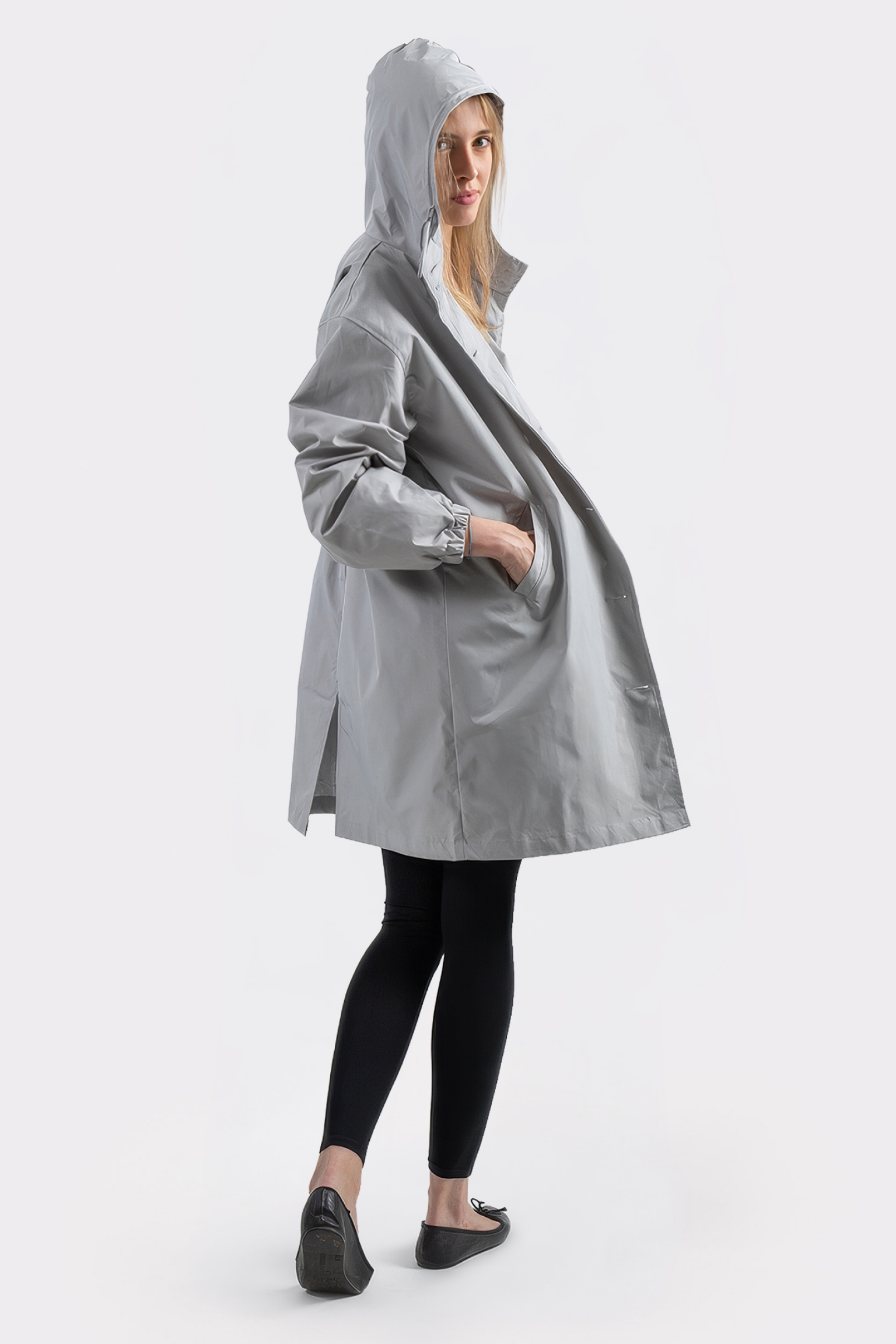 A person models the Icon Windbreaker Rain Jacket in light gray, paired with black leggings and black flats, standing with one hand in the jacket pocket against a plain white background.