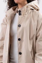A person wears the Icon Windbreaker Rain Jacket in beige, partially unbuttoned over a white ribbed shirt, with their face partly out of frame.