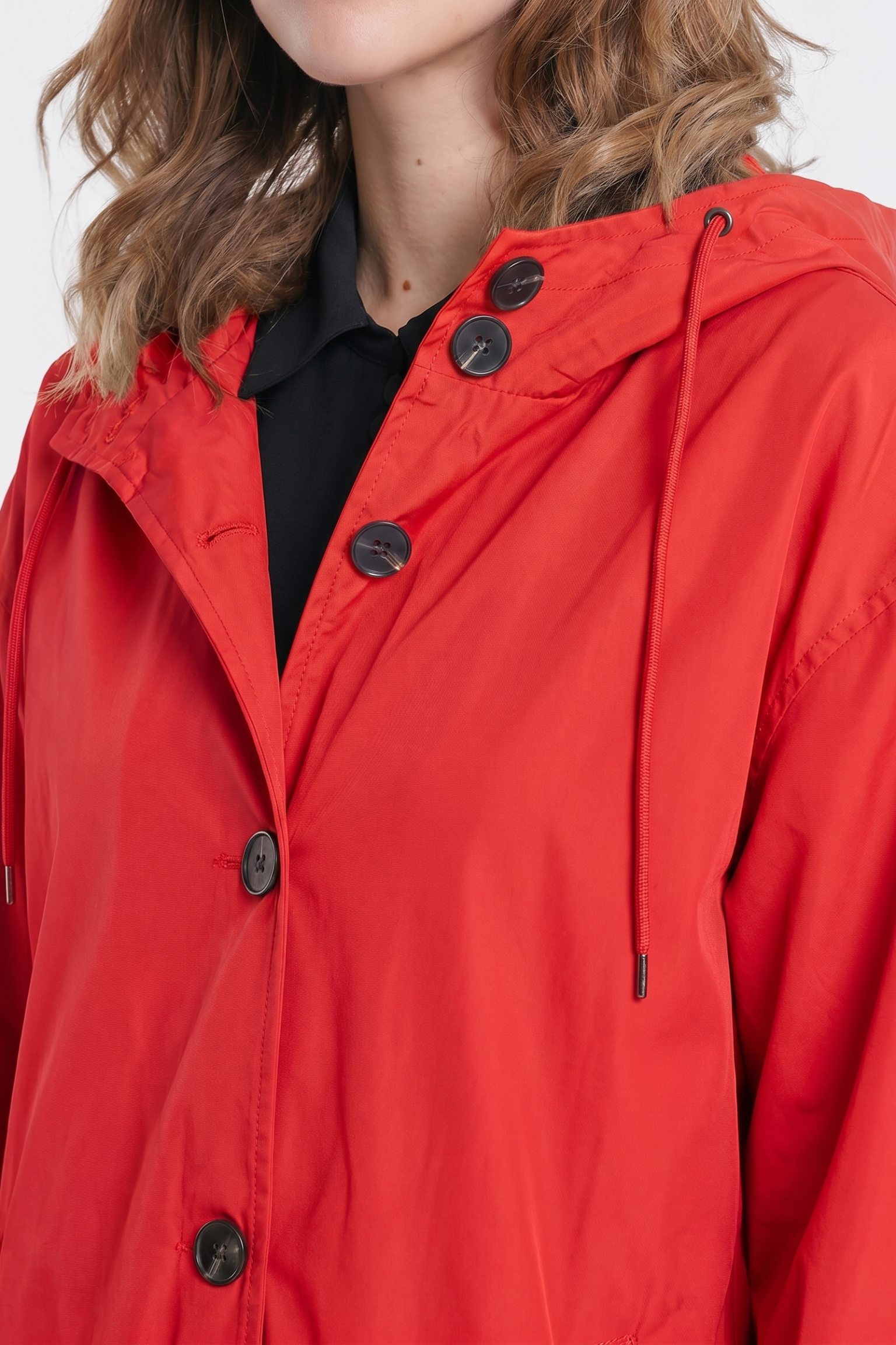 A person wearing the Icon Windbreaker Rain Jacket, a bright red hooded coat with black buttons, layered over a black shirt. Only their lower face and upper torso are visible.