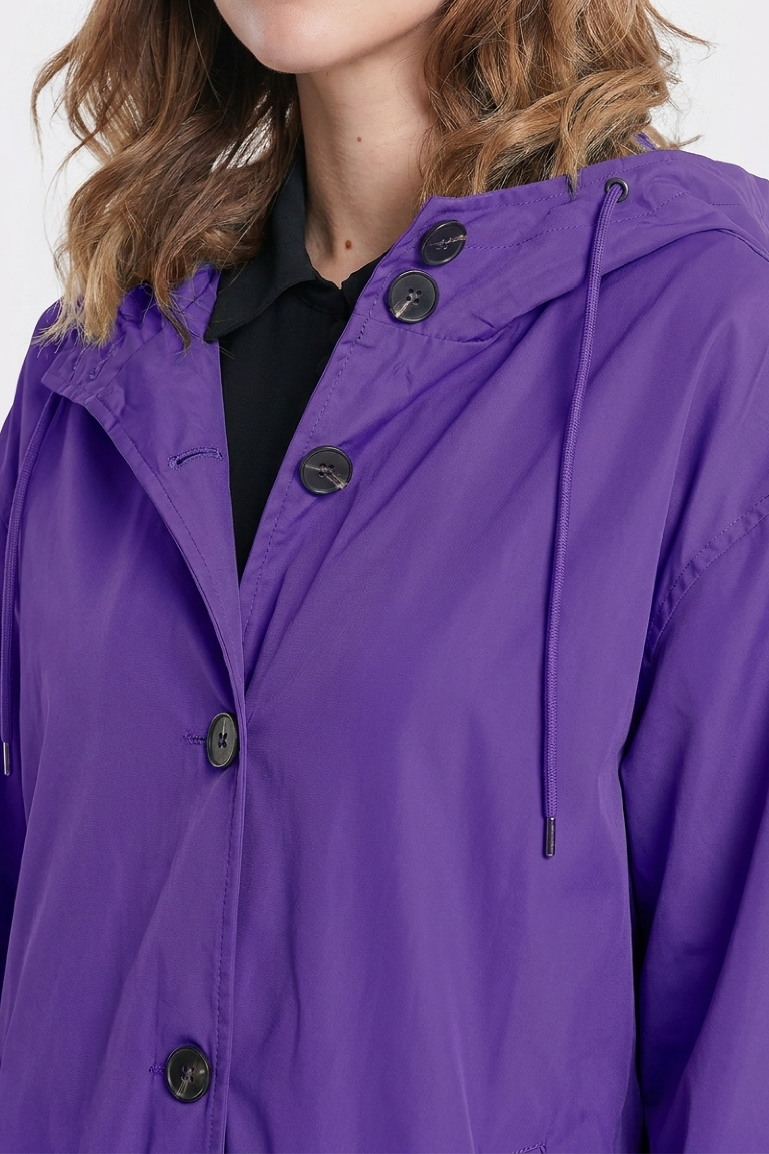 A person wearing the Icon Windbreaker Rain Jacket in purple, featuring a hood and drawstrings, over a black shirt. Only the lower half of their face and upper torso are visible.
