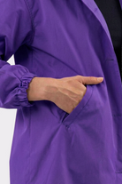 A person wearing the Icon Windbreaker Rain Jacket with elastic cuffs places their right hand into the pocket. The background is plain and light-colored.