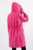 A person is seen from the back touching the hood of an Icon Windbreaker Rain Jacket, featuring a bright pink color and an elastic waistband, against a plain white background.