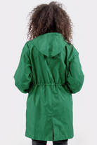 A person with curly hair is seen from the back wearing the Icon Windbreaker Rain Jacket in green, featuring a hood and drawstring waist, standing against a plain white background.
