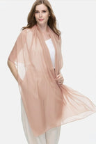 A woman wears the looselyboho Sandstone Dune 100% Cashmere Scarf over a white top and light pants, standing against a plain white background and looking at the camera with a neutral expression.