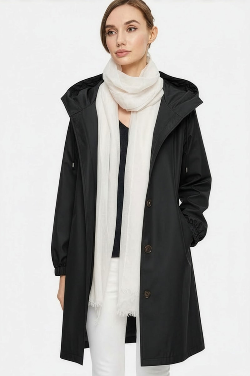 Against a plain light background, a person in a black hooded raincoat, dark top, white pants, and the looselyboho Ivory Whisper 100% Cashmere Scarf embodies minimalist luxury.