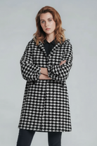 A woman with shoulder-length brown hair stands with arms crossed, modeling the looselyboho HOUNDSTOOTH WINDBREAKER over dark pants and a black top, against a plain light gray background.