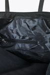 The image shows the inside of a black, lightweight "The One" Waterproof Travel Bag by looselyboho. There is a small zippered internal pocket on one side. The interior fabric has a smooth, slightly shiny texture. Two dark shoulder straps are partially visible at the top edges, perfect for the sophisticated traveler.
