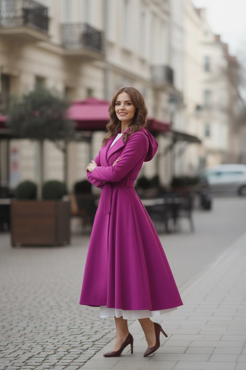 A woman stands on a cobblestone street in the looselyboho Water-Repellent Rain & Shine A-Line Hooded Raincoat in bright purple, layered over a white dress with matching heels. She smiles with arms crossed; outdoor seating and buildings are behind her.