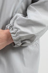 Close-up of a person’s arm wearing a looselyboho ICE GRAY WINDBREAKER with the hand partially visible. The jacket sleeve, made from water-resistant material, has an elasticated cuff gathered at the wrist. The background is plain and light-colored.