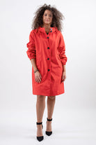 A person with curly hair wearing a bright red, stylish CRIMSON RED WINDBREAKER by looselyboho with black buttons stands against a plain white background. They are also wearing black ankle-strap heels and minimal jewelry.